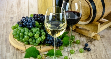 Weingläser und Weintrauben vor einem Holzfass auf Holzboden